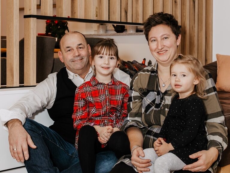 Die Gastgeber des Luxus-Chalets im Bayerischen Wald sitzen auf der Couch und lächeln in die Kamera.